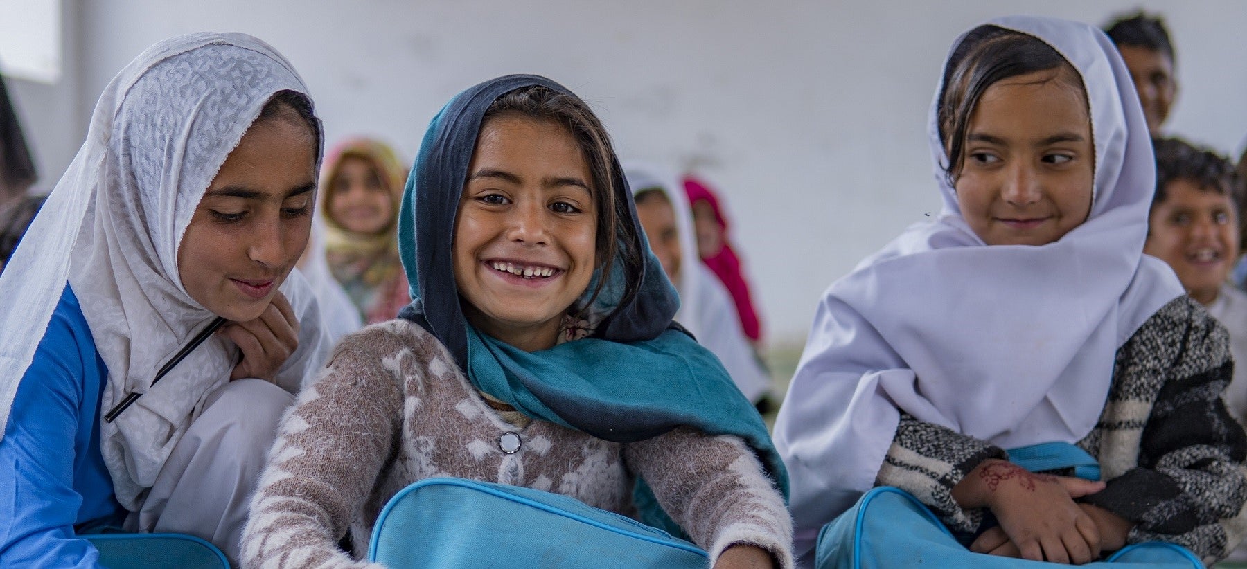 Three school girls from Pakistan smiling at the camera with their new UNICEF school bags.