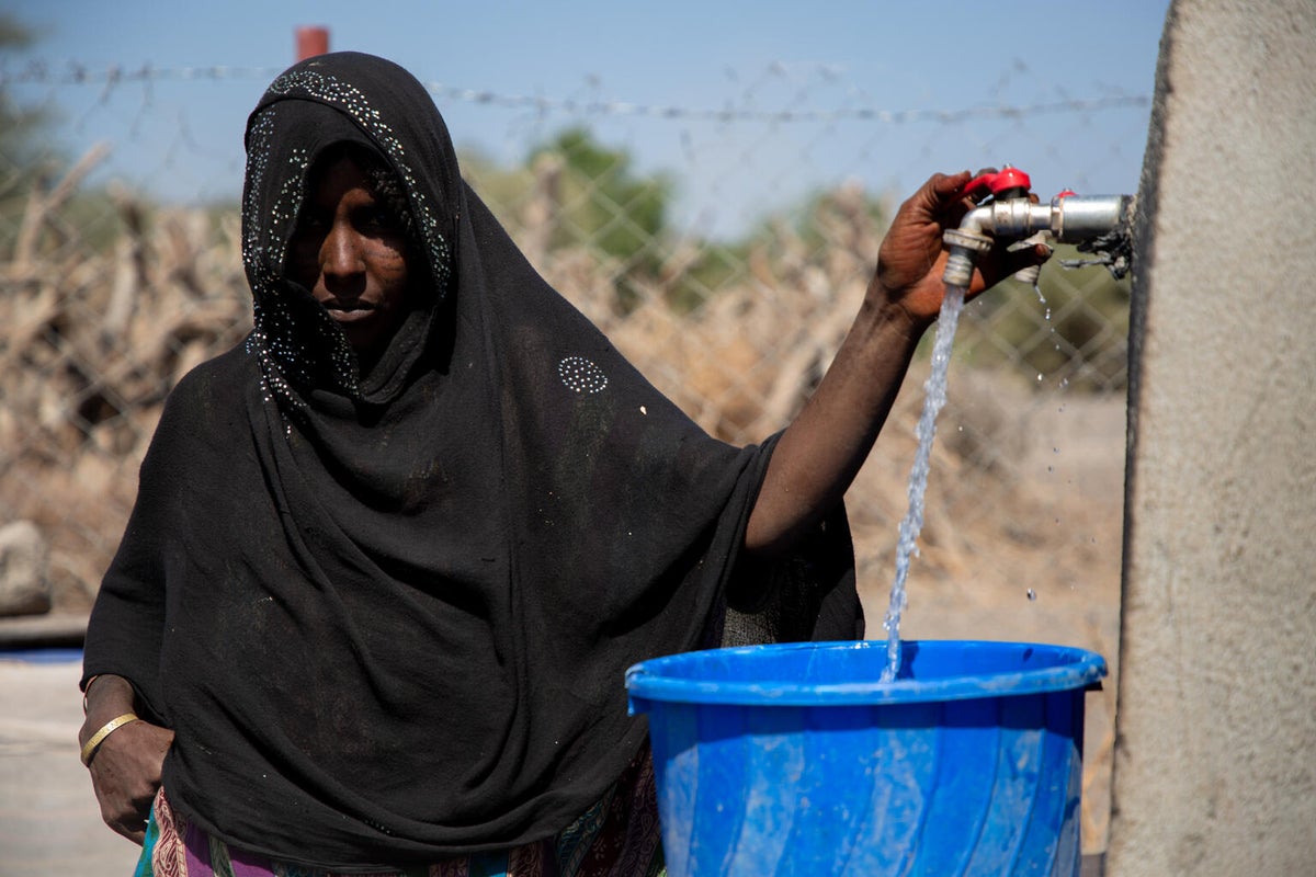 A woman is filling a bucket in what looks like a communal water tap.