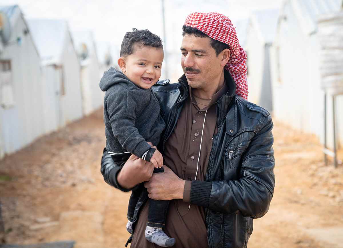 One-year-old Mohammad smiles to the camera as he is held in his father's arms in a refugee camp in Jordan.