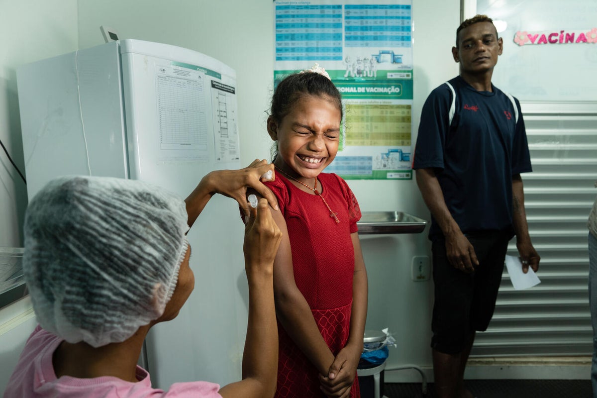 A girl scrunches her face as she gets a needle vaccination in her arm