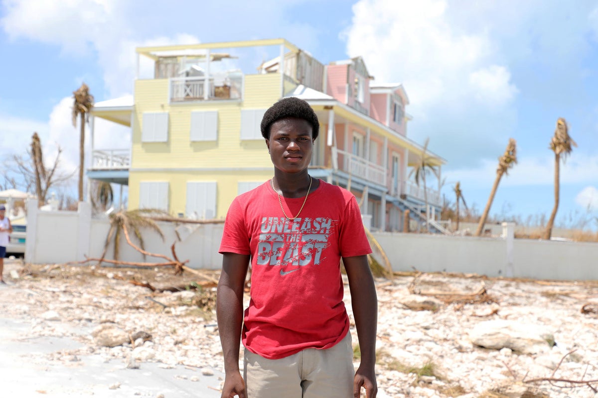 A young man posing to the camera. Behind him, the landscape looks devastated by winds.