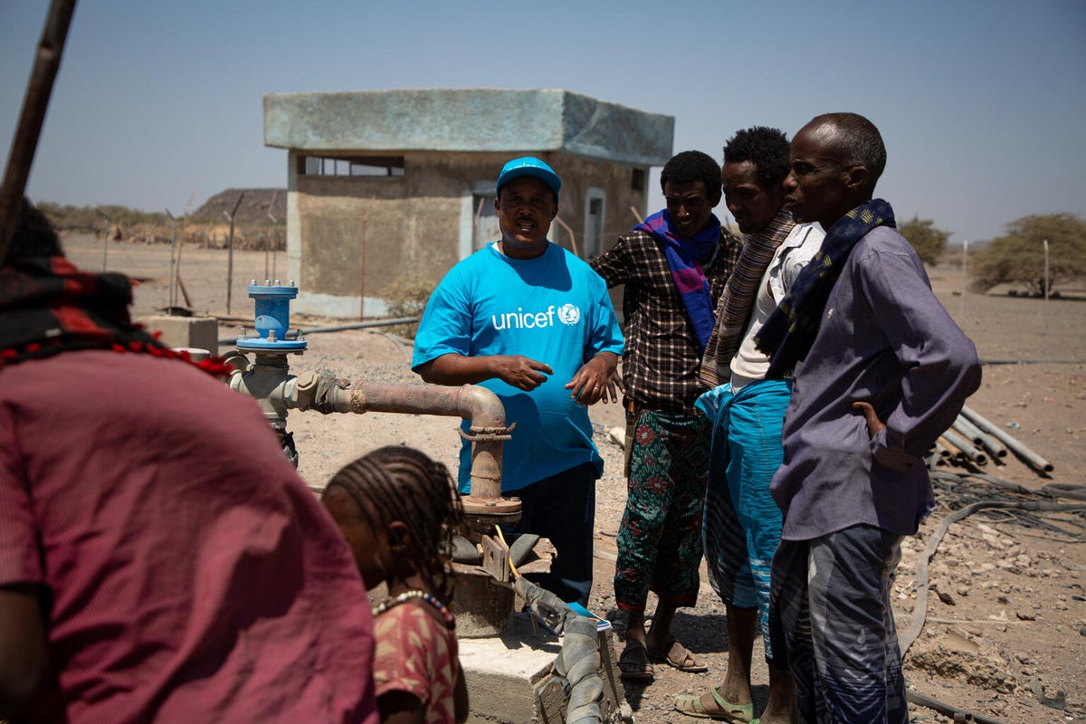 A group of men gather around a water supply. One of them has a UNICEF shirt.