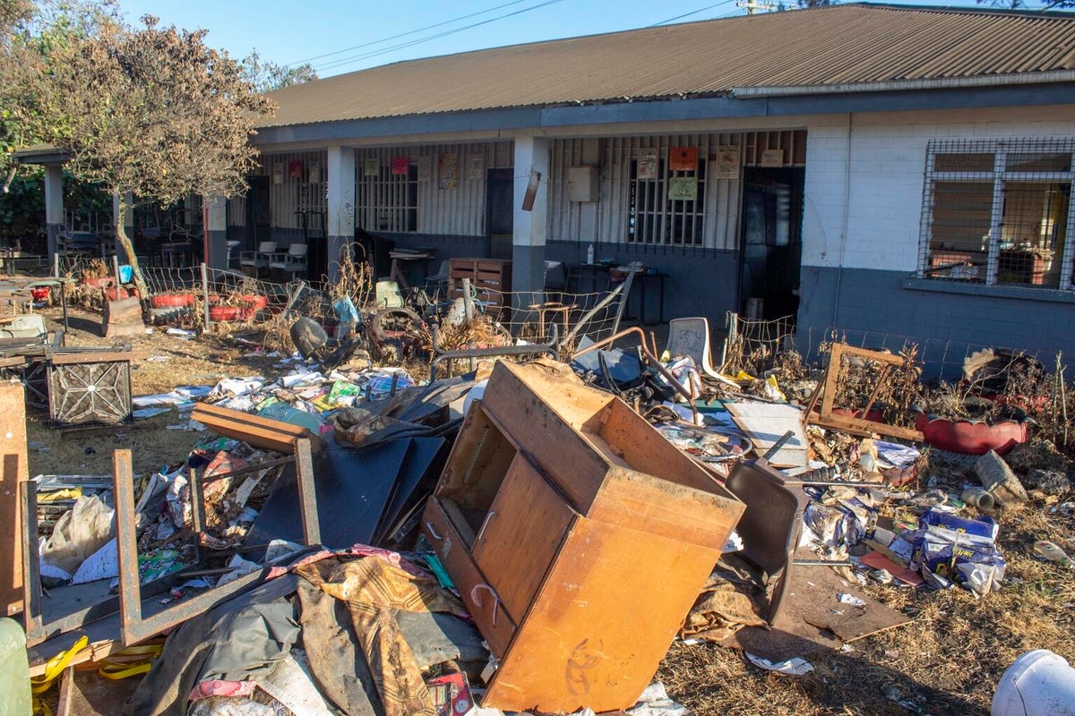 On the background, a school. On the foreground, broken furniture and more debris.