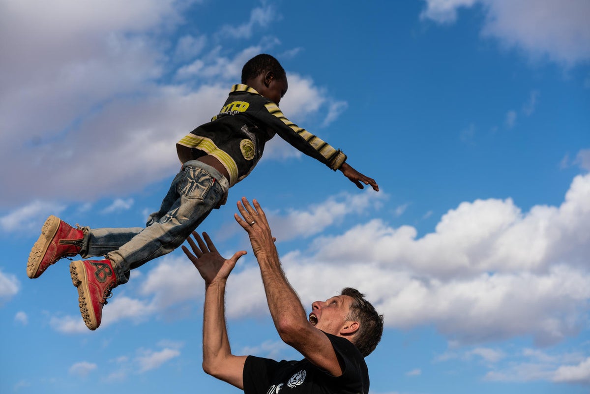 A man is playing with a boy and he lifts him in the air.