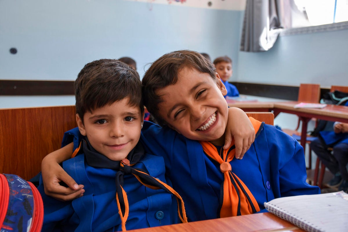 Two Syrian boys sitting in a classroom and smiling at the camera