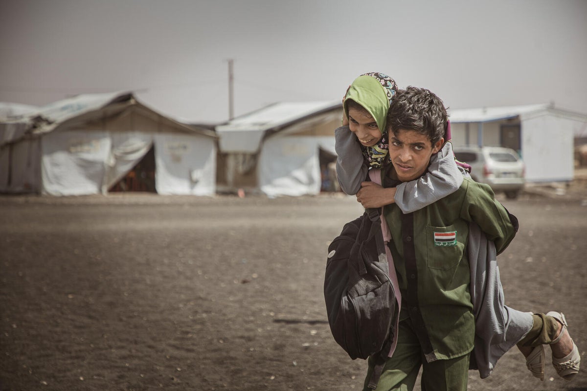 A young boy carries his sister on his back as he walks to school. 