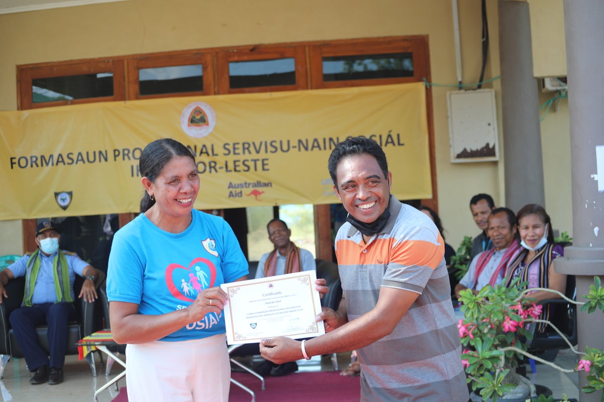 A woman is passing a certificate to a recent male graduate of the program