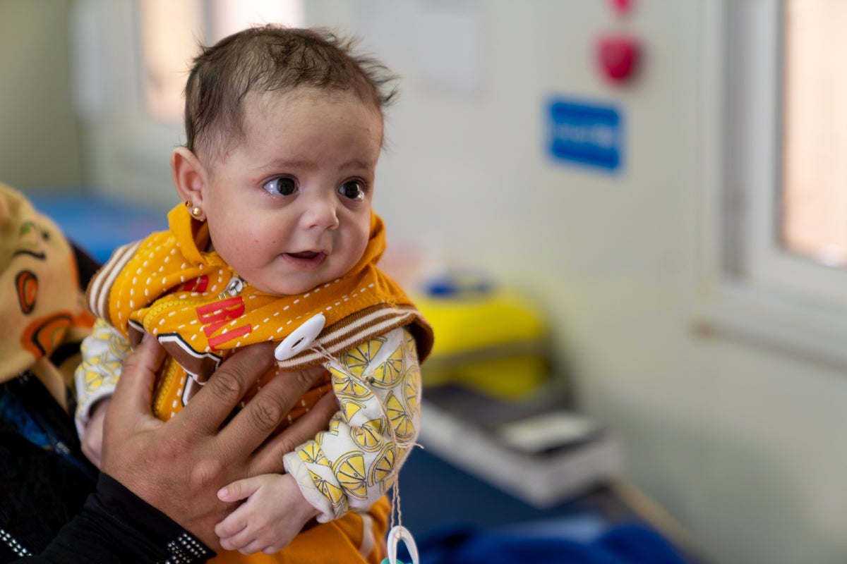 Baby in yellow jumper in her mothers arms. 