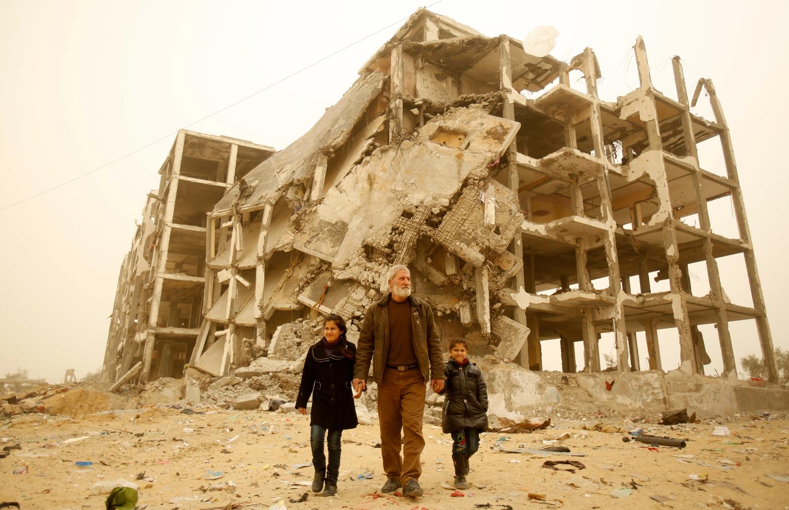 Grandfather, with grandchildren, in front of the rubble of their town
