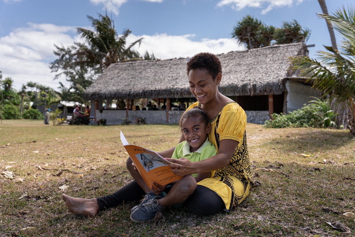 A five-year-old boy is sitting at his mum's lap while they read a book together.