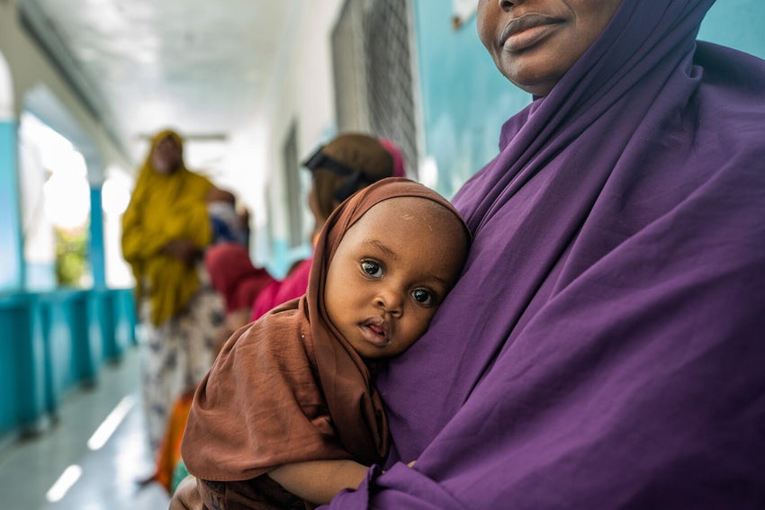 A baby sits on her mother's lap at a healthcare clinic in Somalia. 