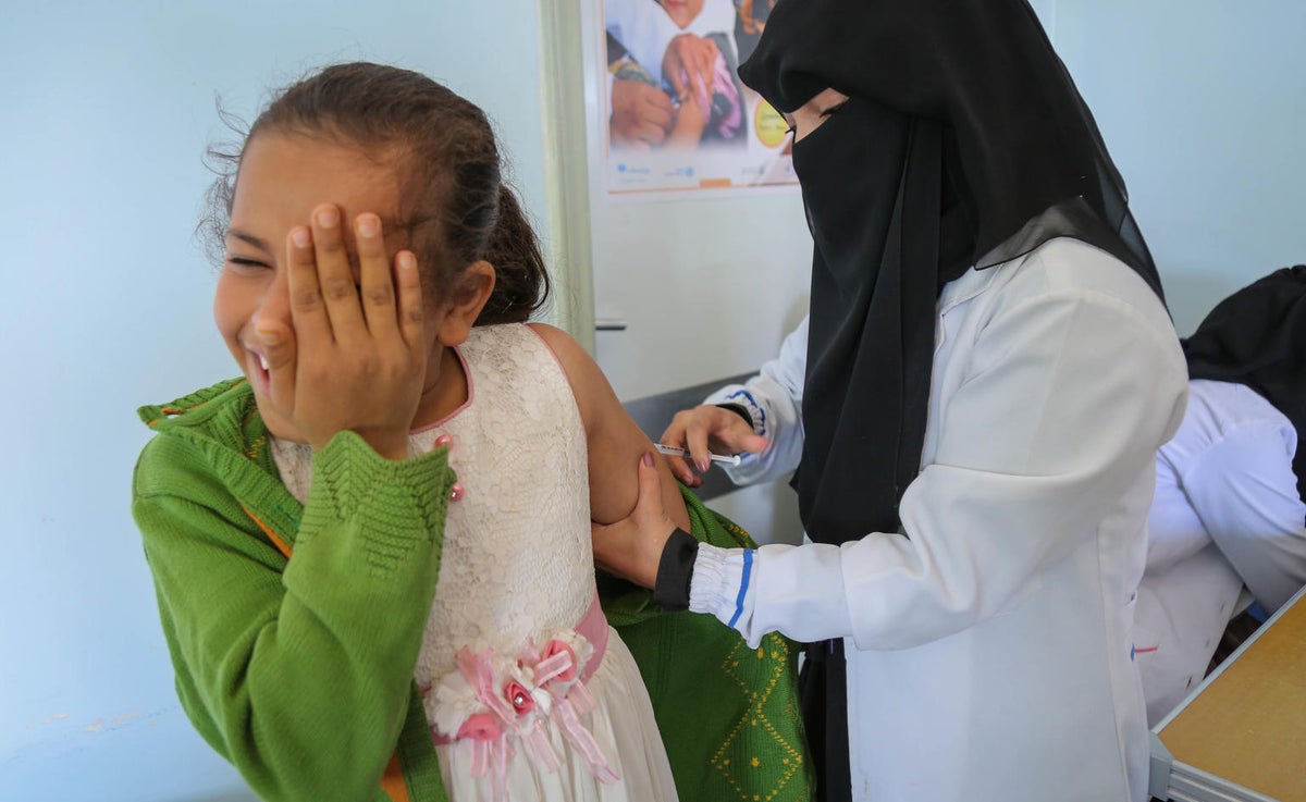 A girl is getting a vaccine on her arm and she's looking away from it. She is approximately seven years old.