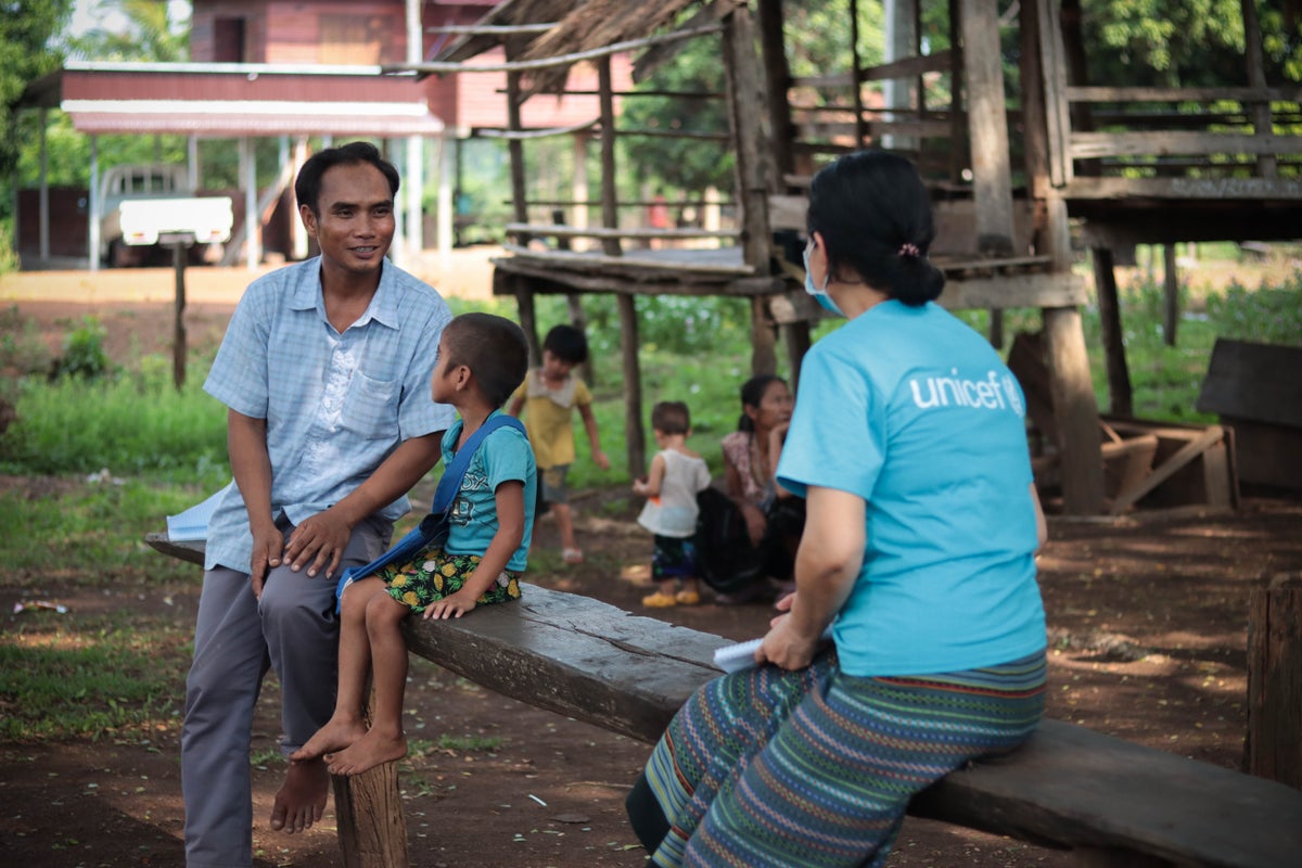 A UNICEF worker sits with a father and son to talk about early childhood education.