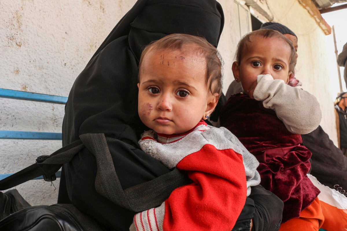 A woman in a burqa is holding a baby who is looking at the camera. There's another baby held by another woman behind them.