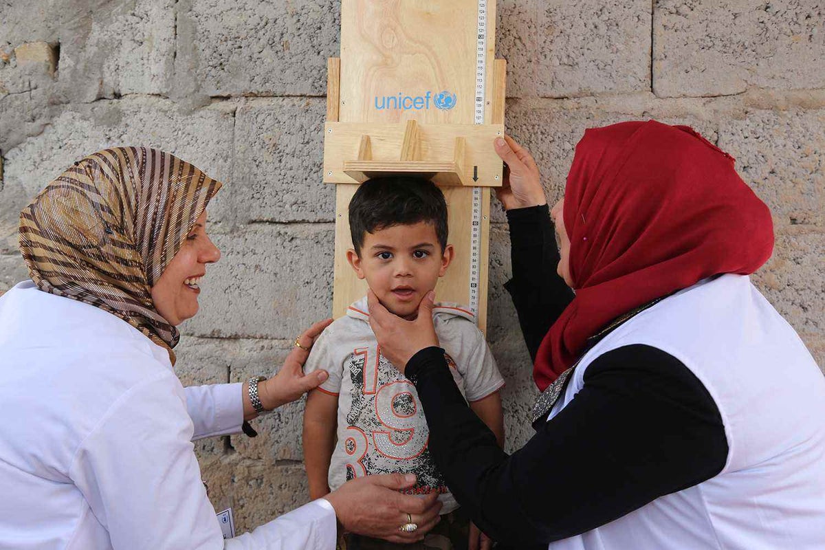 Three-year-old Tyjan is measured by health workers in Al-Takya Al-Kasnazaniya camp  