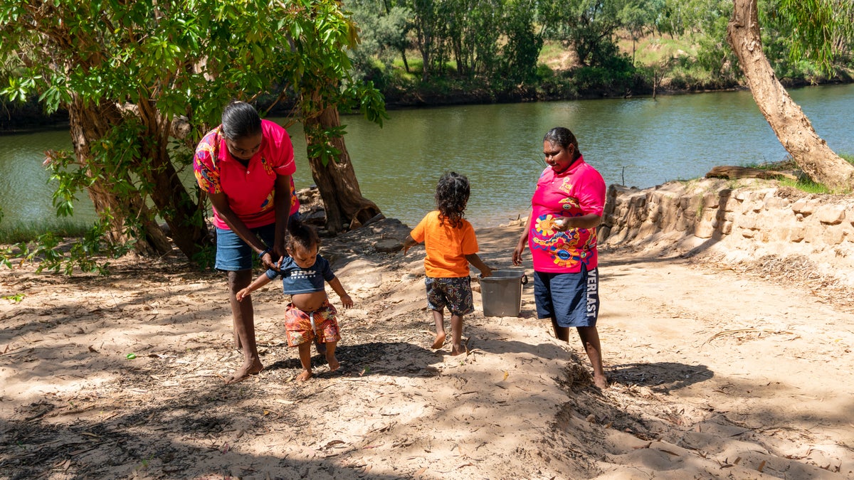Two instructors teach two young children how to use a handwashing station next to the river. 