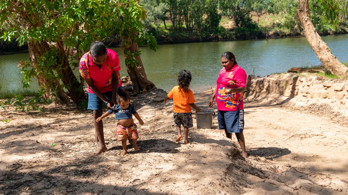 Two instructors teach two young children how to use a handwashing station next to the river.