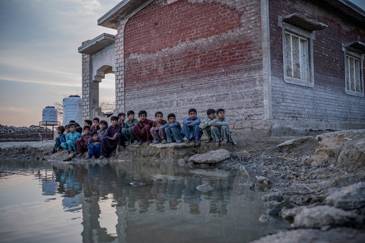 Children sitting in front of a dilapidated building, surrounded by flood water