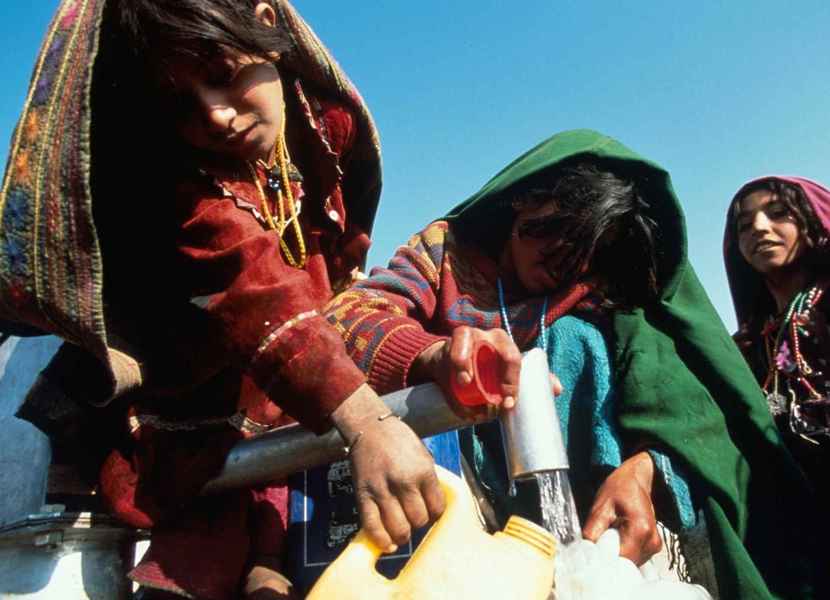 Girls fill jerrycans with water at a hand-pump, in the Maslakh camp, near Herat in 2000. 