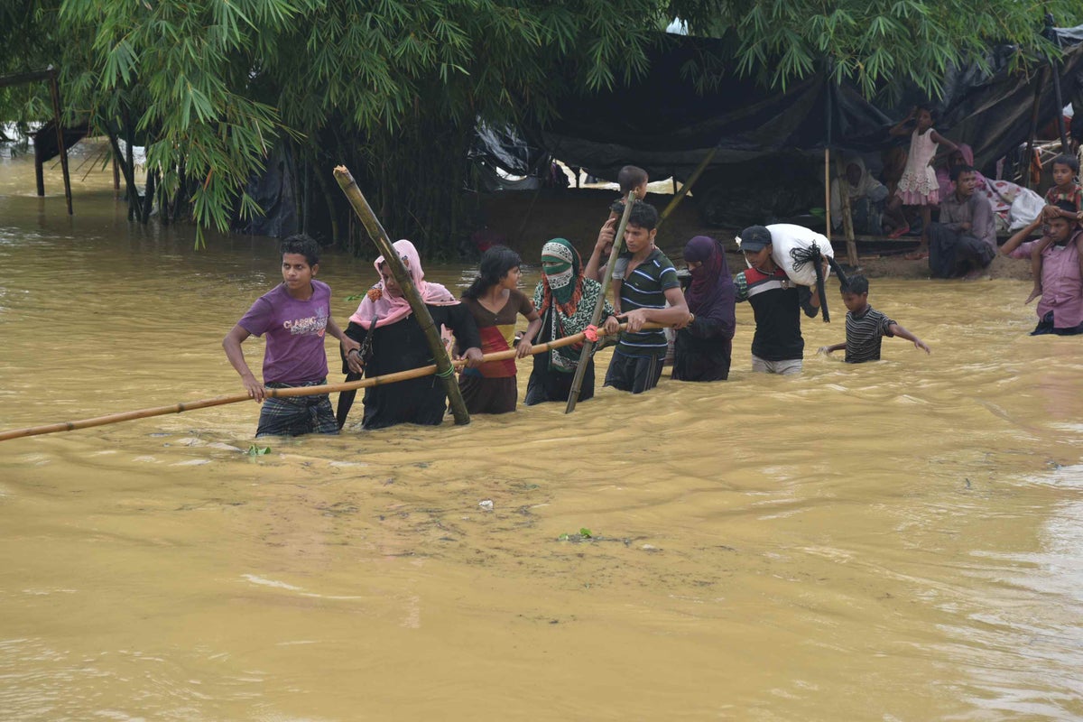 Families attempt to cross a makeshift bamboo bridge over a flooded river.