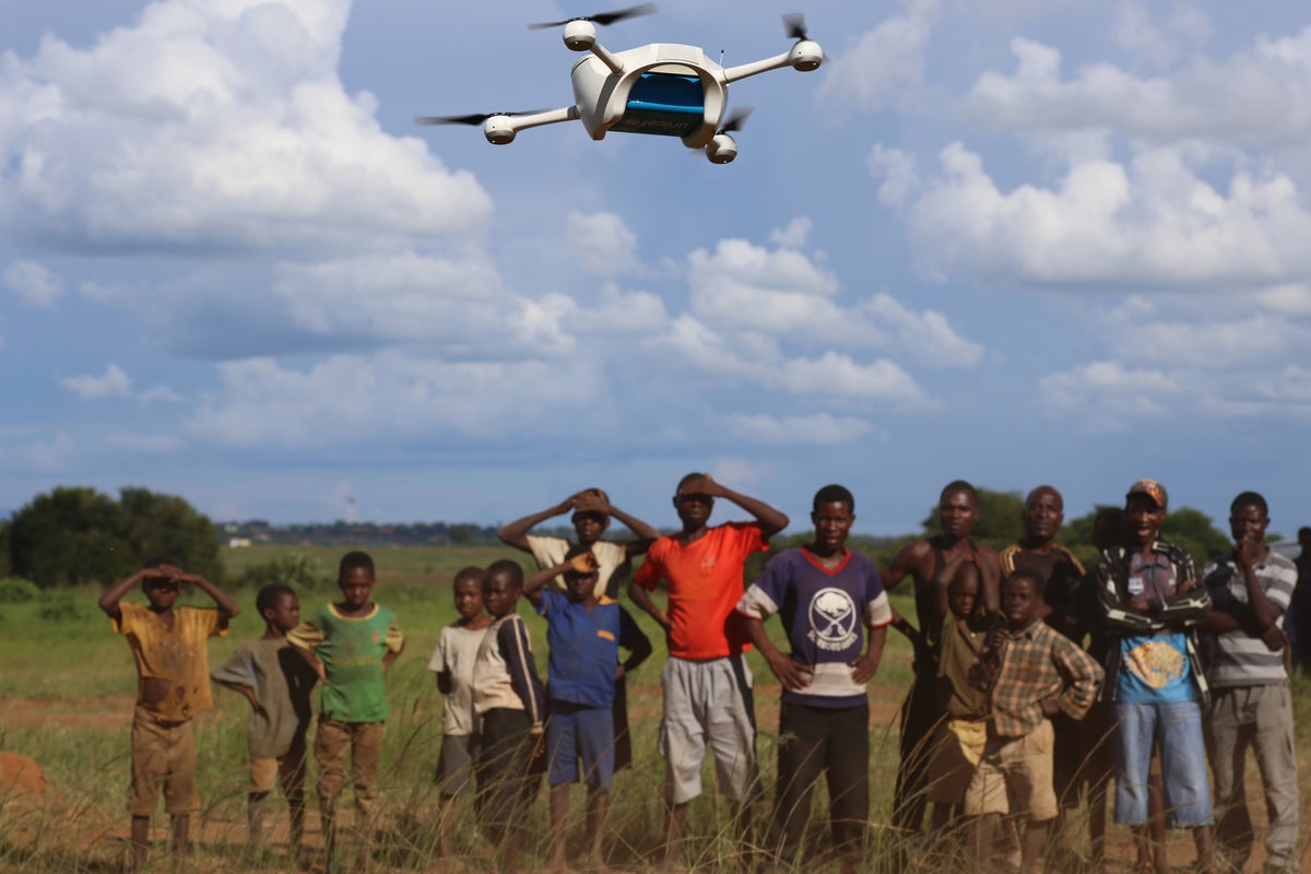 A large group of children look at a drone when it's landing.