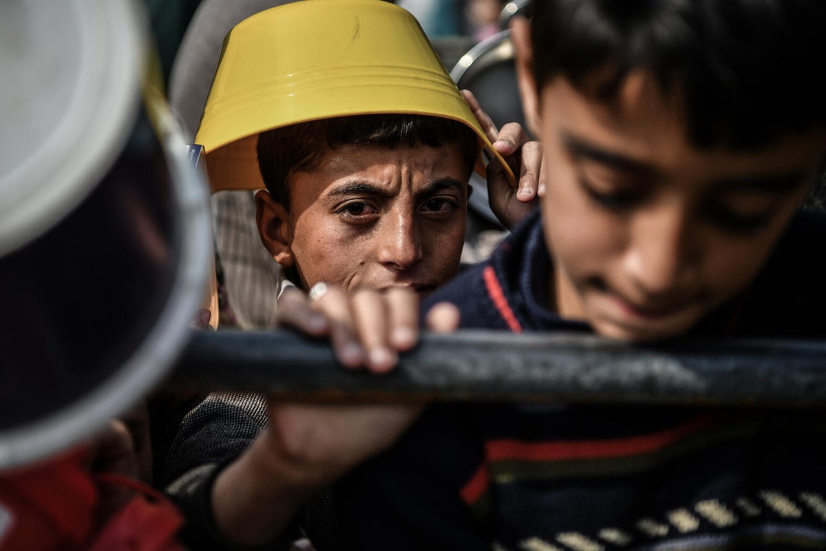 A young boy holding a bucket waits in line for food in Gaza. 