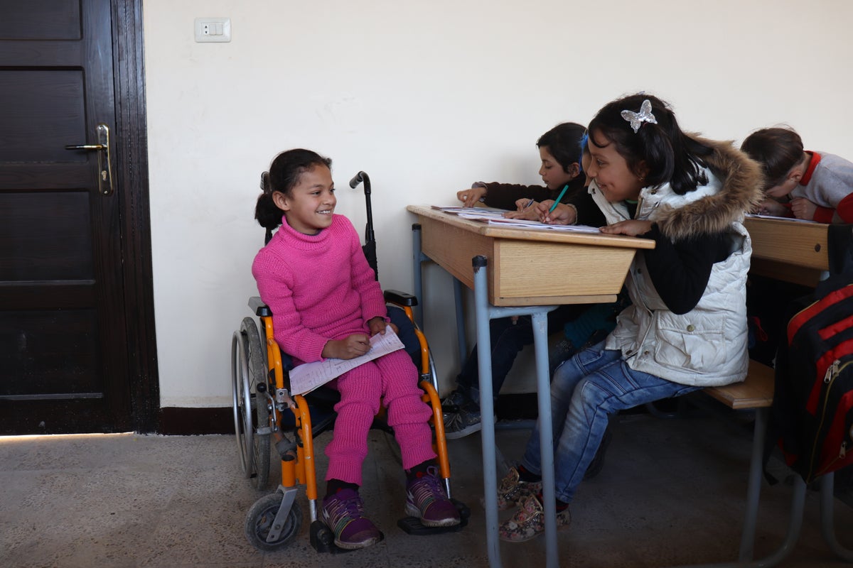 Girl in pink sits in a wheelchair in classroom.