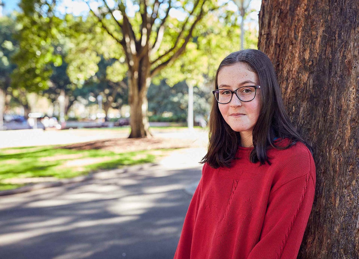 girl in red jumper stands next to tree