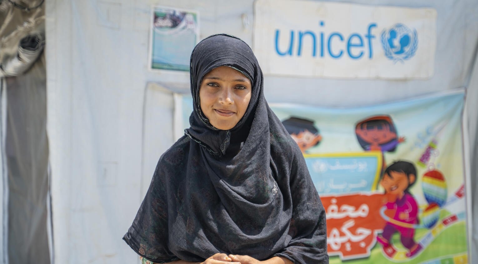 A young girl standing in front of a UNICEF tent in Pakistan.