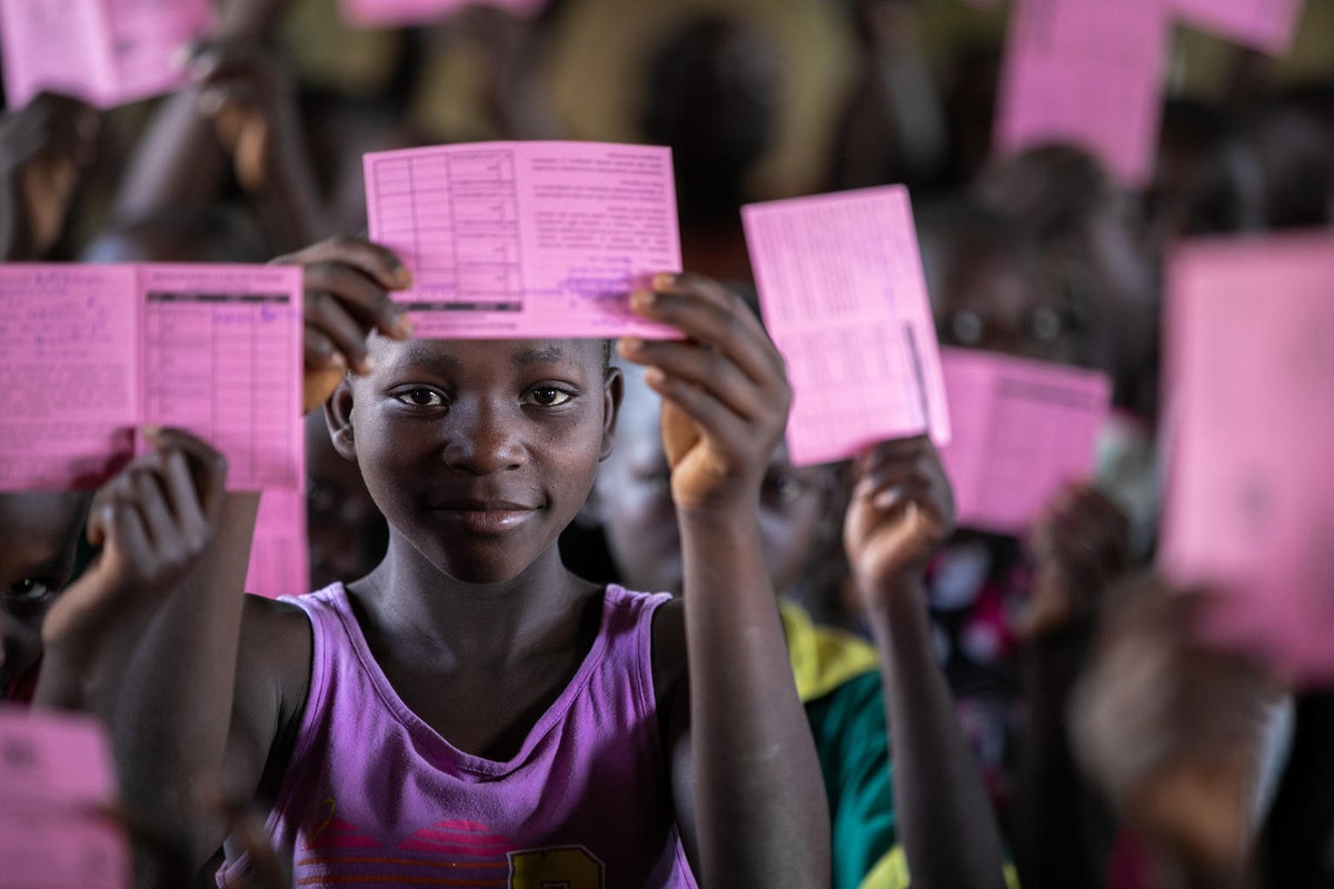 A young child is holding a vaccination certificate and showing it to the camera