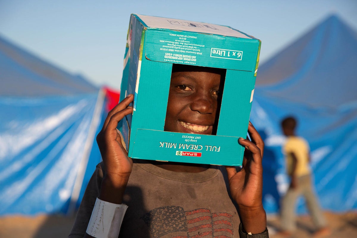 A young boy is playing, wearing a cardboard box with a hole as a helmet.