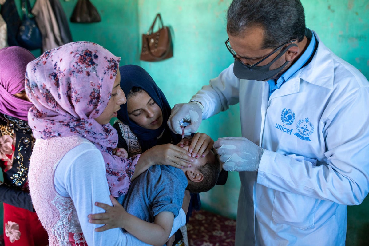 A health worked is providing a droplet vaccine to a boy while two women hold the baby.