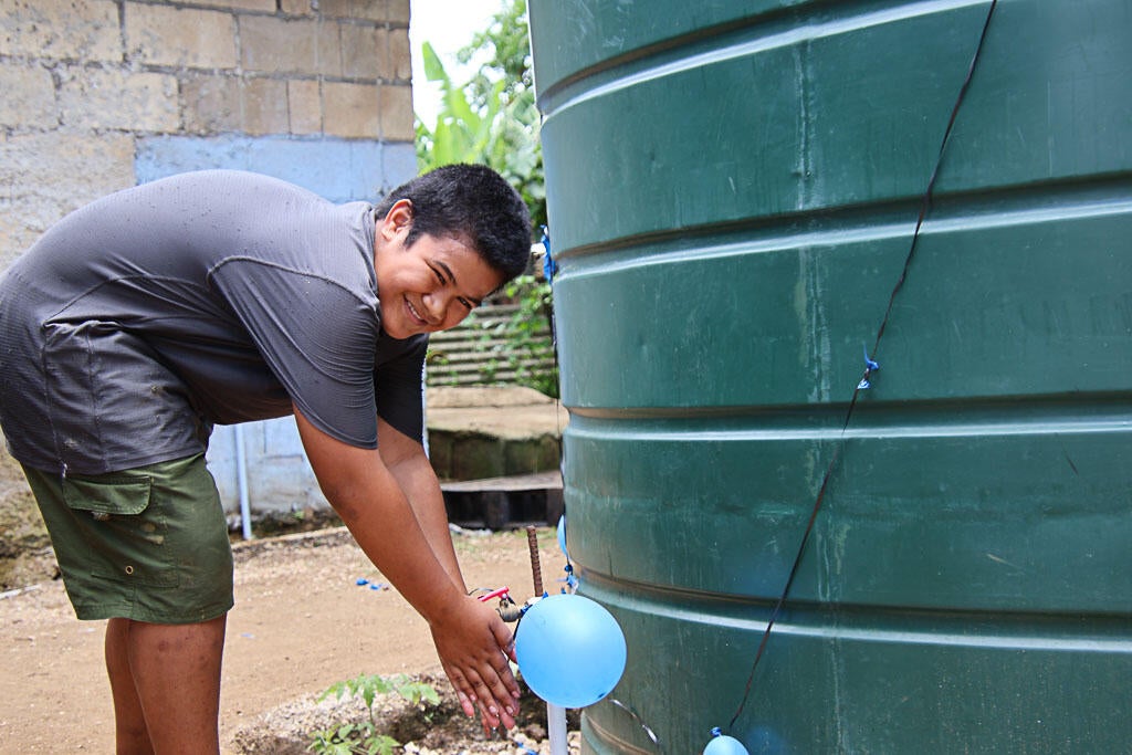 Paula, a 12-year-old Tongan boy is washing his hands at their new water tank.