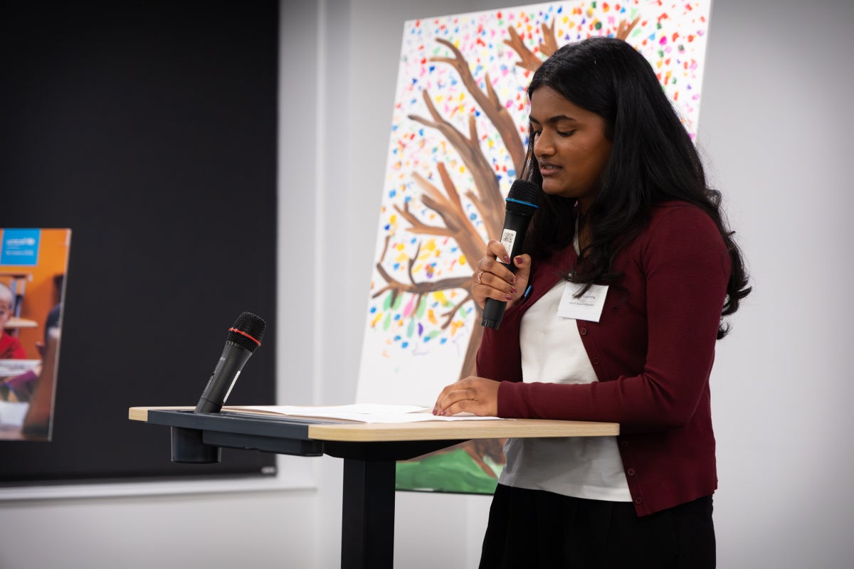 A young woman holds a microphone as she speaks at a lectern.
