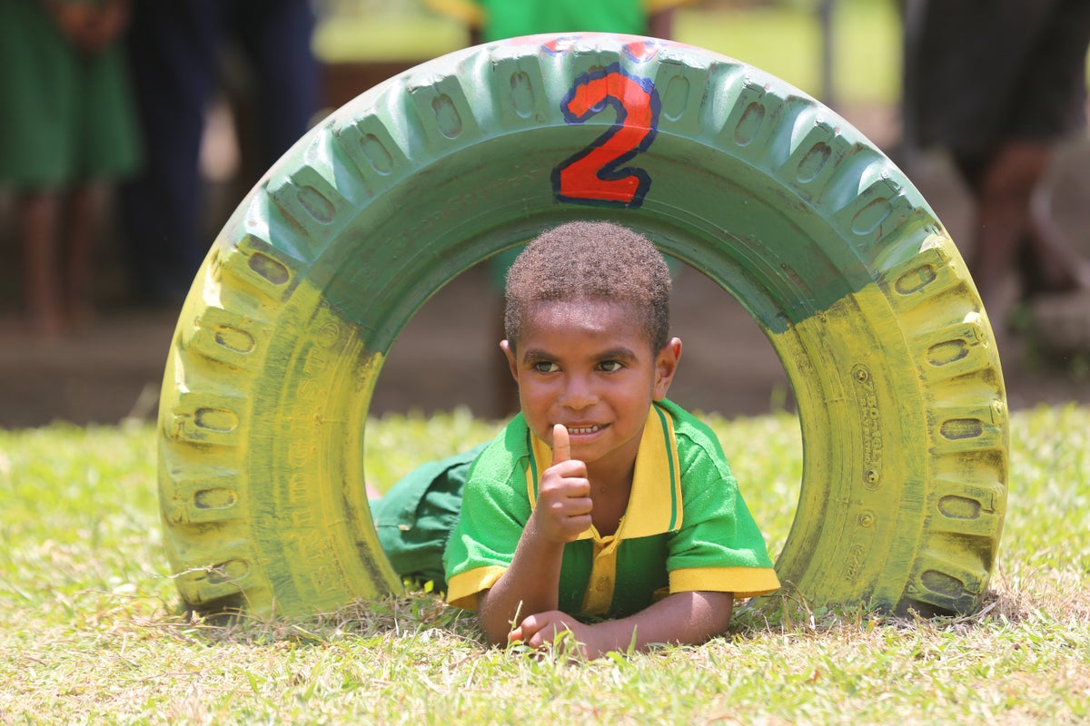 A young boy is playing in a playground. He is going through an old tyre that is colorfully painted.