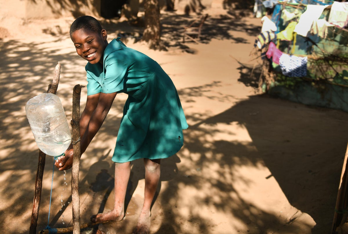 A young smiling girl washes her hands using a makeshift tap in Malawi. 