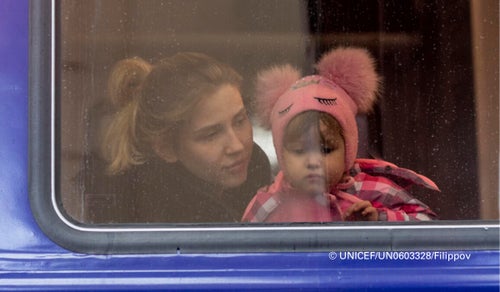 In Ukraine, 2022, a little girl peers out from a window as she waits inside an evacuation train to Poland, at Lviv train station. 