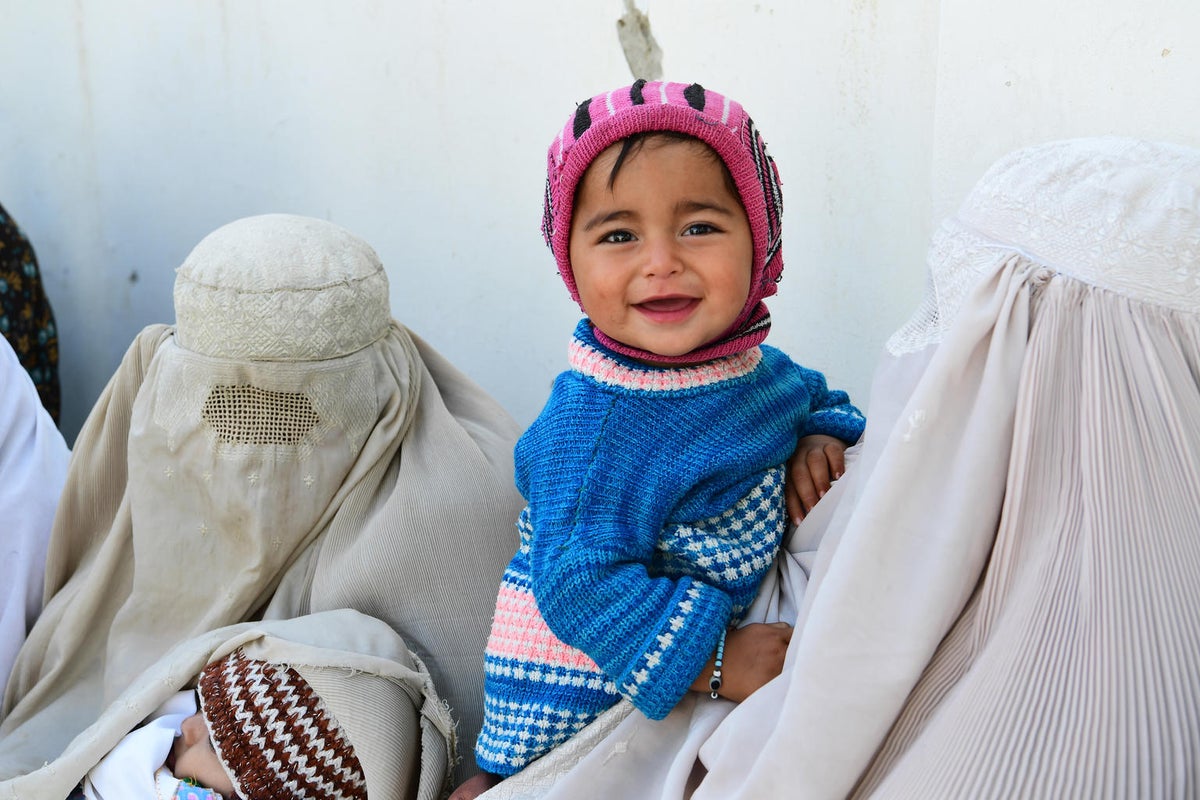 A toddler smiles at the camera. He is held by a woman in a burqa