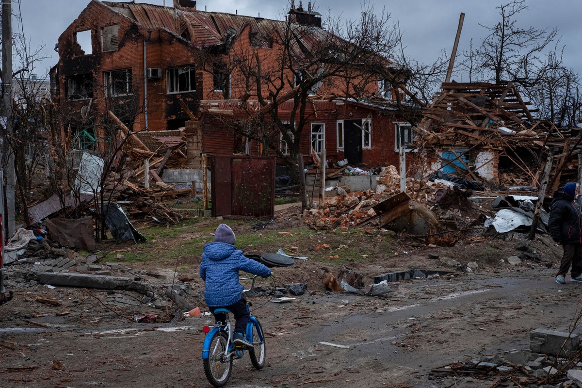 A young child sitting on their bike staring at the ruins of their home. 