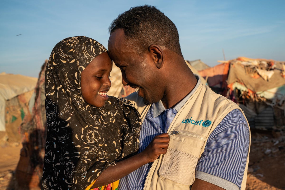 A man is holding a girl in his arms. They are smiling and touching foreheads.