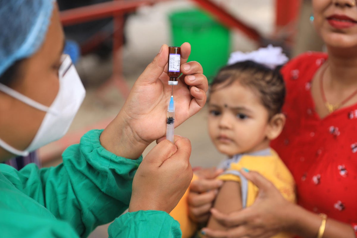 A health worker is drawing a vile to prepare a vaccine while a young girl is looking at her in the background.