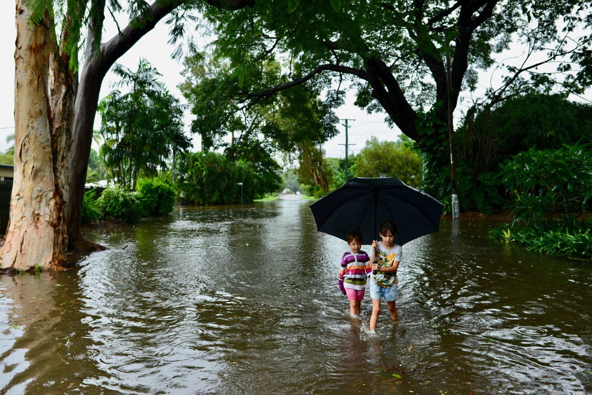 Two children standing under an umbrella wade through floodwaters 