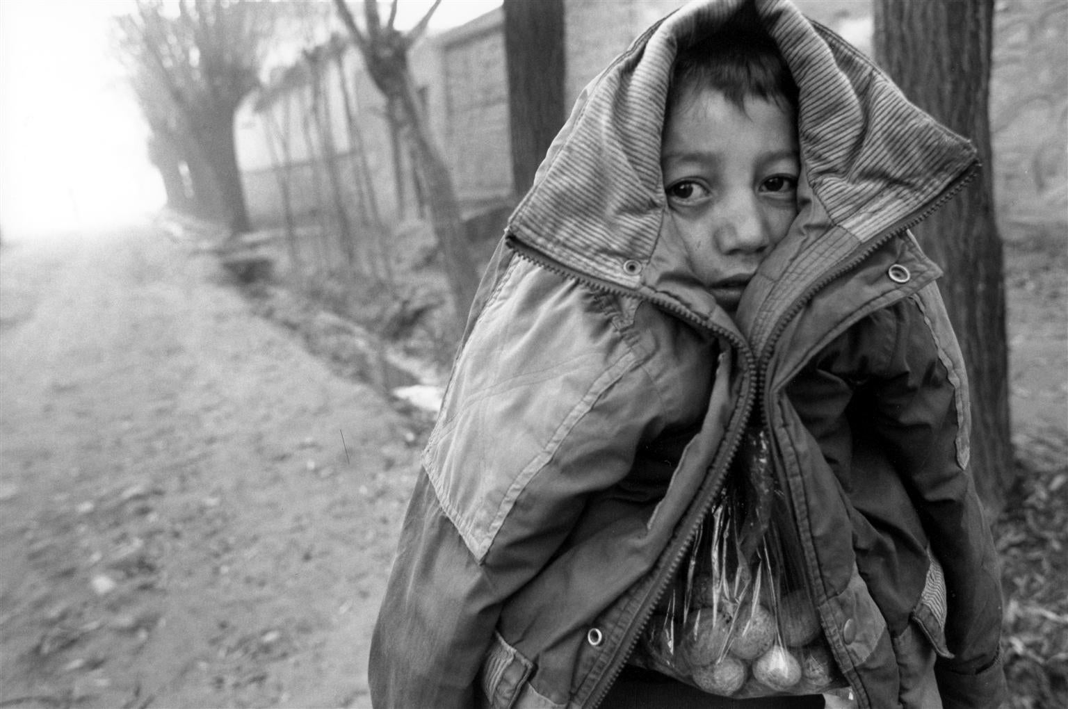 His coat pulled up over his head to protect him from the cold, a boy carrying a bag of nuts walks on a street in Faizabad