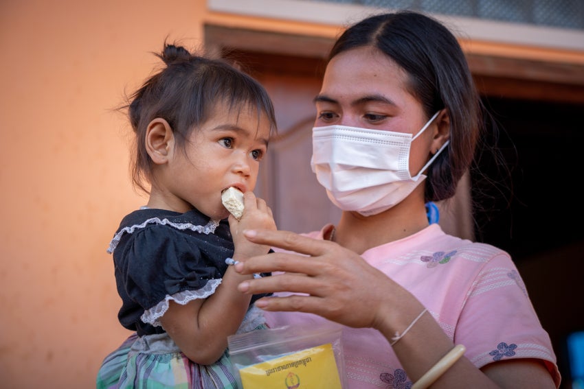 Mother holding baby, eating RUTF