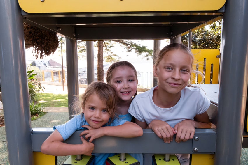 A group of three young children pose for a photo in a playground.