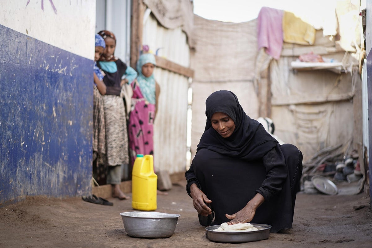 A mother of four children, Aml prepares dough to make bread as two of her children and a niece look on.