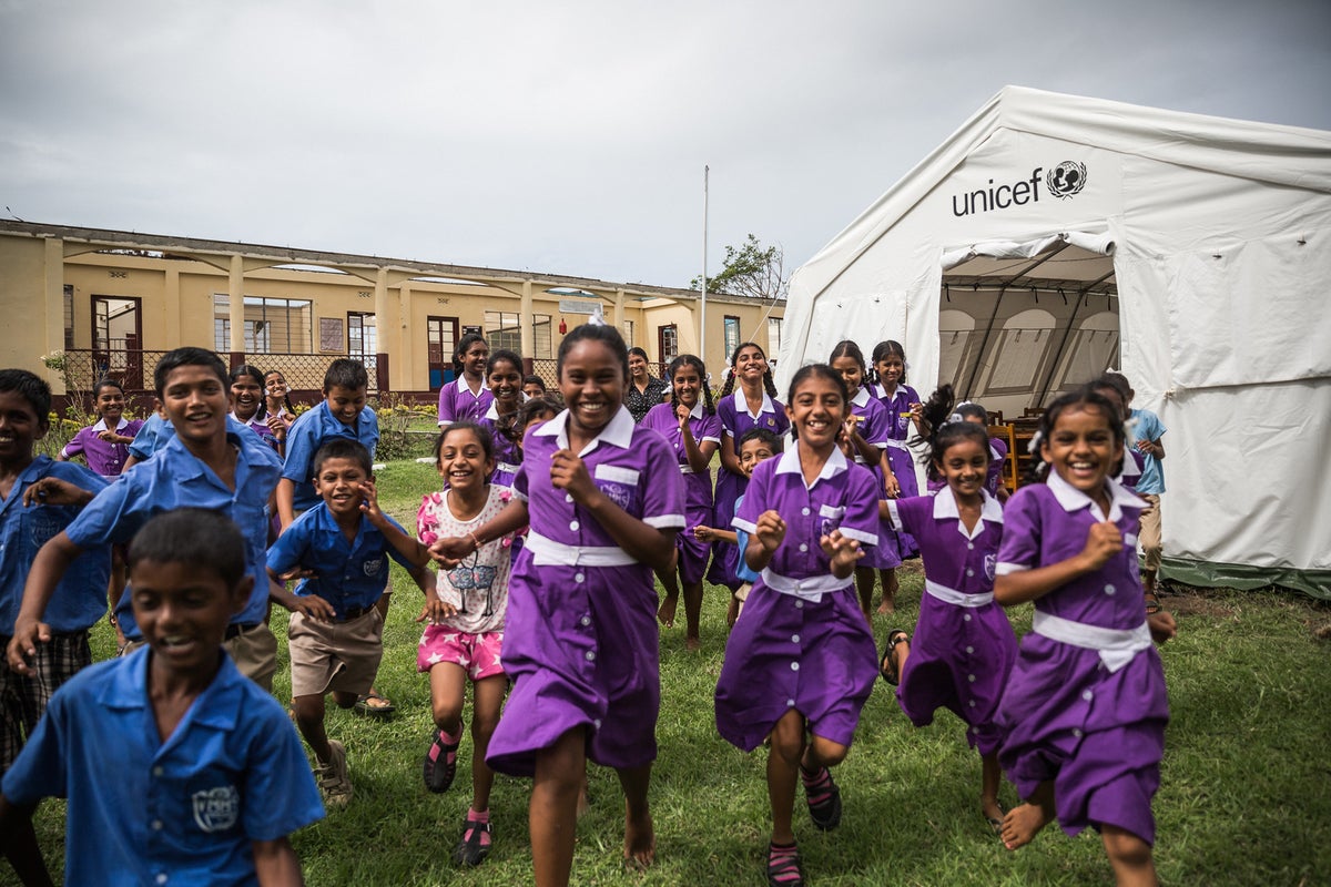 A group of boys and girls in school uniforms are running towards the camera and smiling