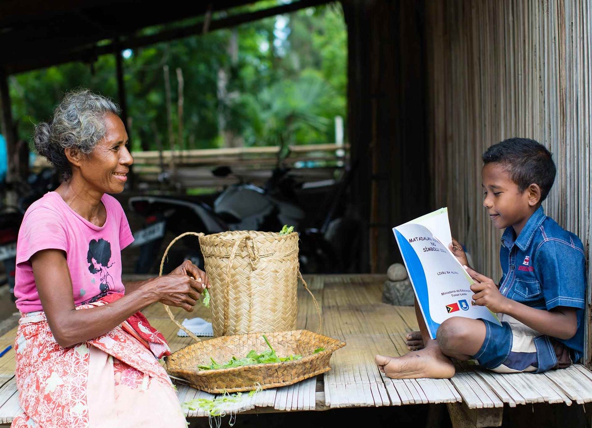 A boy reads as his grandmother looks on in Timor-Leste. 