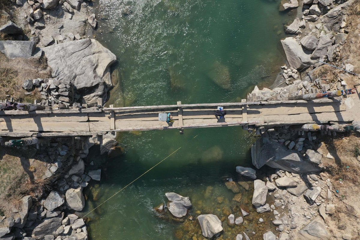 Two men cross a timber bridge across a river in the middle of the mountain.