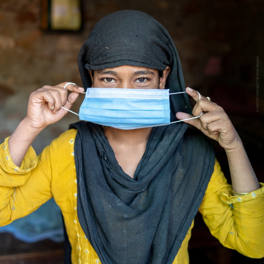 A girl in India holding a face mask across her face.